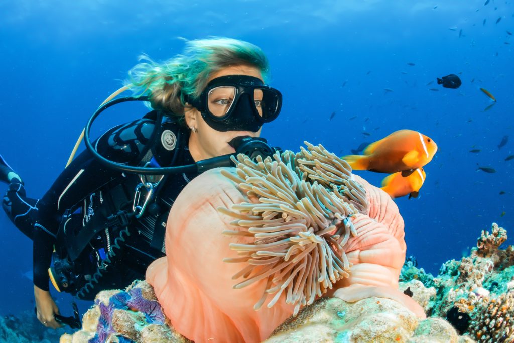 Female scuba diver behind a coral reef and some fishes