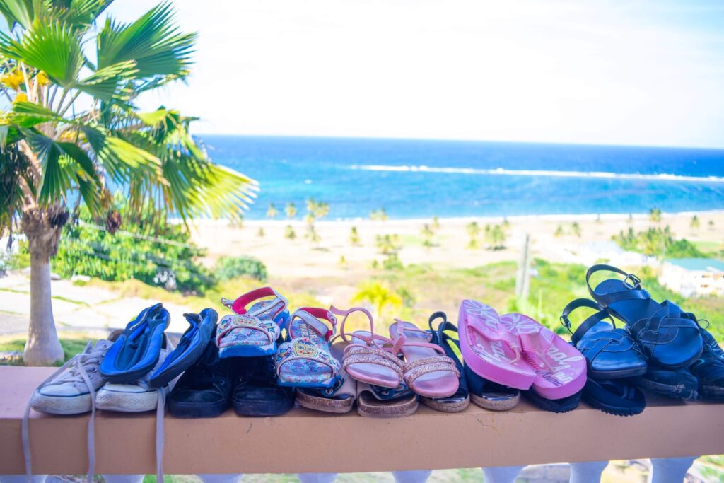 A selection of shoes that were packed to move abroad pictured on a wall overlooking the sea with a palm tree in the background