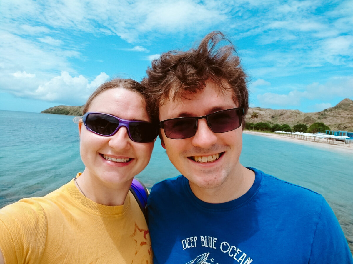 Lewis and Steph stood in front of a beach taking a day trip to Nevis to stave off island fever.