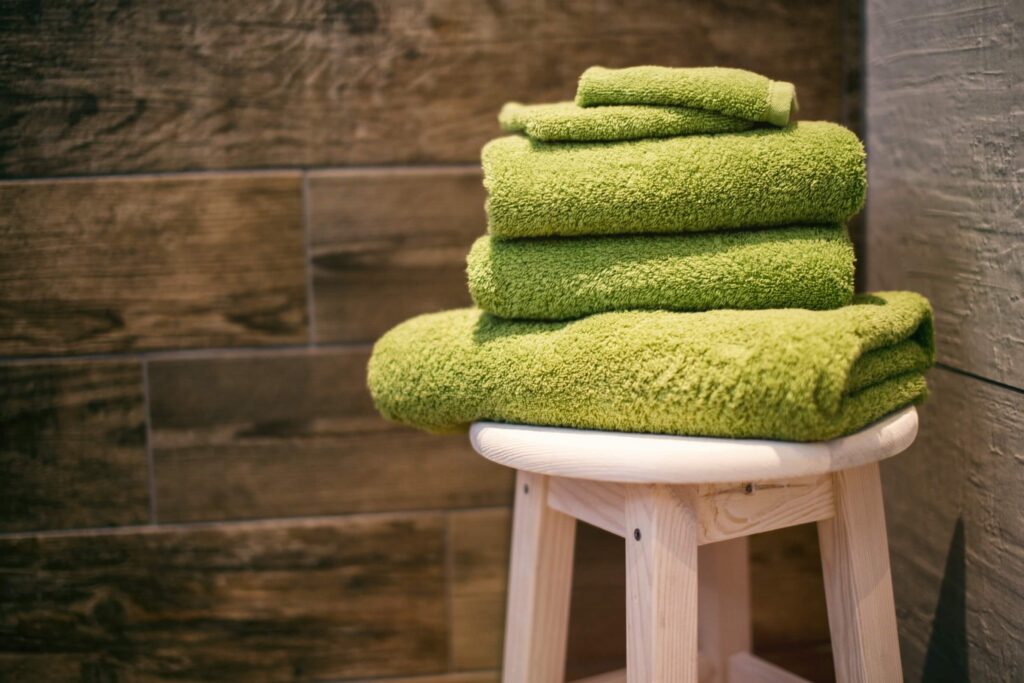 A neat pile of green towels on a wooden chair in a bathroom
