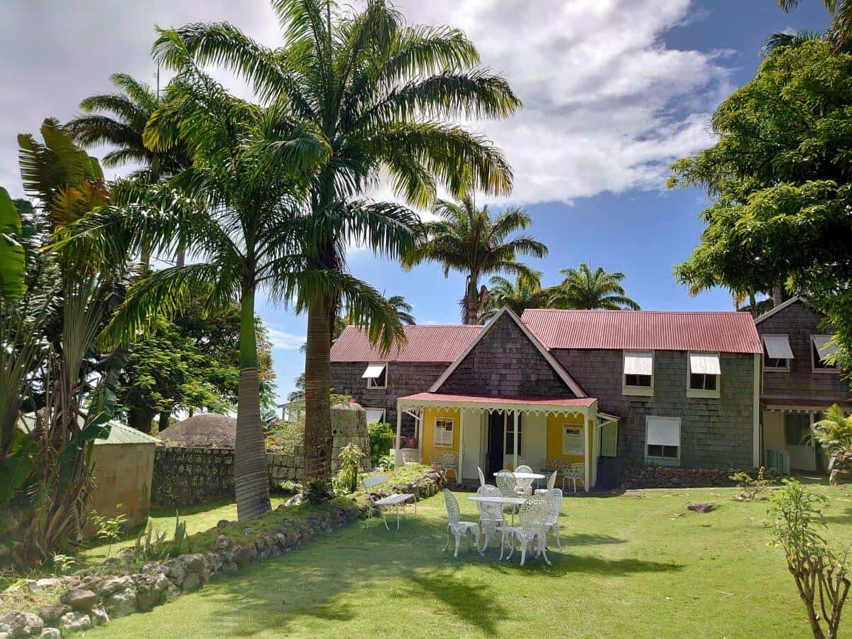 The Hermitage plantation Inn Nevis, an old wooden building in the caribbean surrounded by palm trees with a front lawn and a blue sky