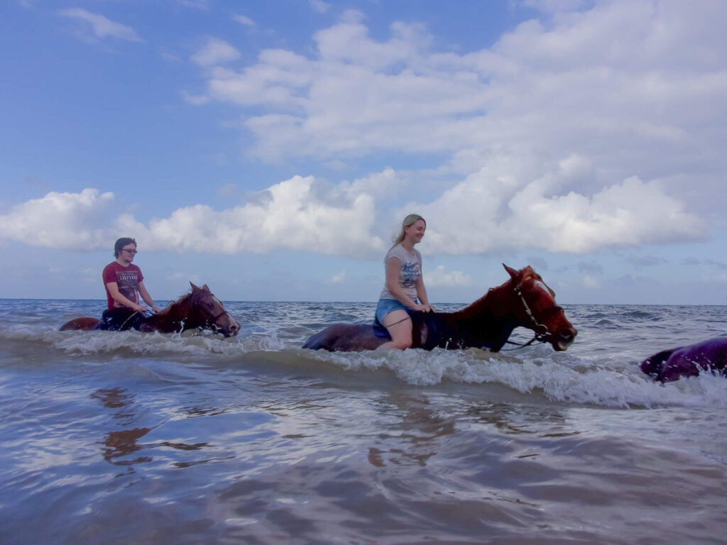 a couple riding two horses in the sea in Jamaica on honeymoon