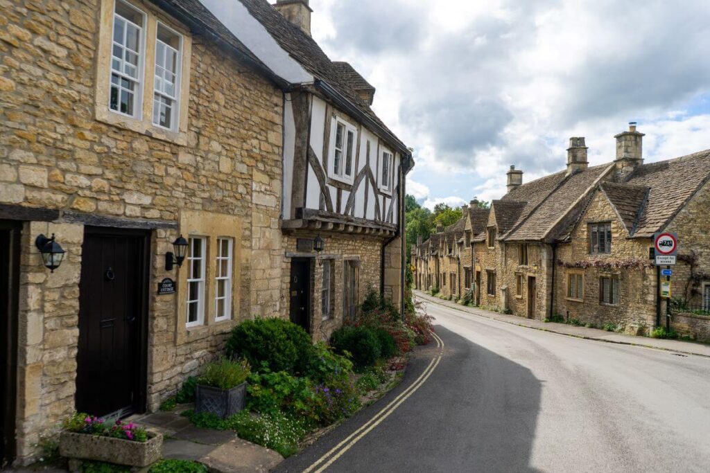 A small street in Castle Combe in The Cotswolds in England lined with stone built houses and flowers